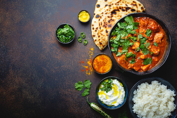 Traditional Indian dish Chicken tikka masala with space for text. Spicy curry meat in bowl, basmati rice, bread naan, yoghurt raita sauce on rustic dark background, top view, close up, copy space  - Photo, Image