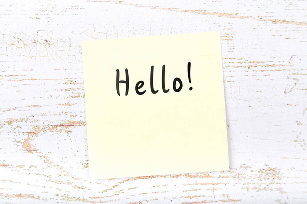 Yellow sticky note on wooden desk with handwritten text hello - Foto, Imagem
