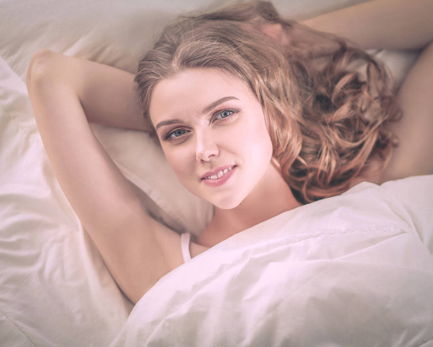 Pretty woman lying down on her bed at home. - Foto, afbeelding