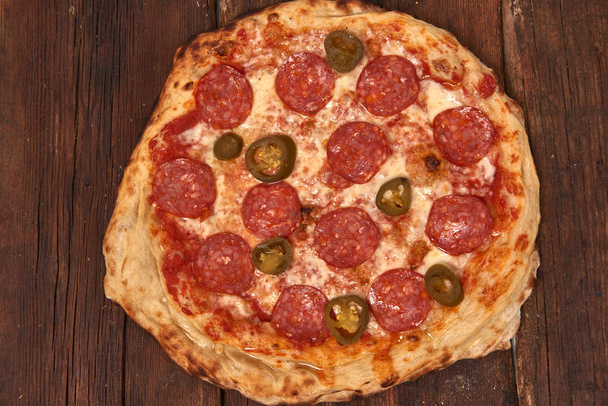 Домашняя свежая вкусная пицца для гурманов с острой салями и халапеньо перец, вкусная итальянская пицца изолирована на деревянном столе, Закрыть с избирательным фокусом
 - Фото, изображение