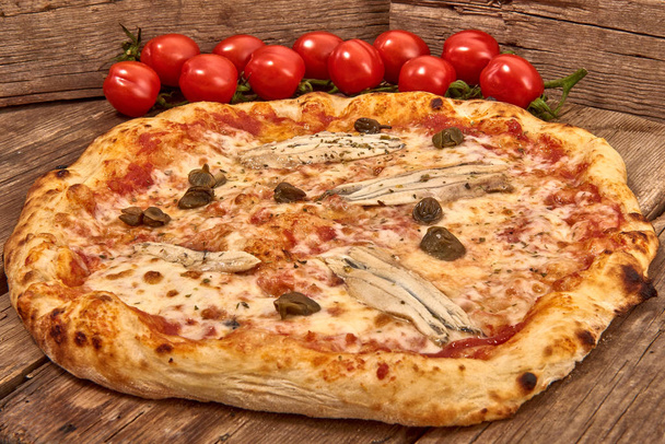 Domowej roboty, świeże wyśmienite pizza Romana odrobina anchois, kaparami i oregano, pysznej pizzy włoskiej na białym tle na drewnianym stole, z bliska - Zdjęcie, obraz