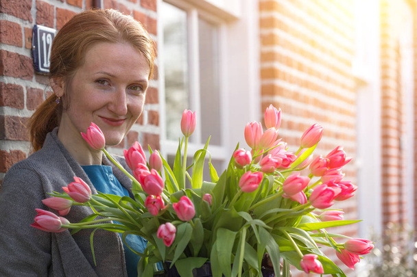 smiling happy girl holding a vase with pink tulips near with a traditional Dutch house. The Netherland - Foto, imagen