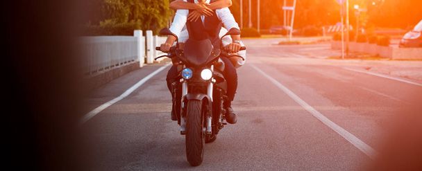 Jong koppel ridind motorfiets op weg van de stad bij zonsondergang. - Foto, afbeelding