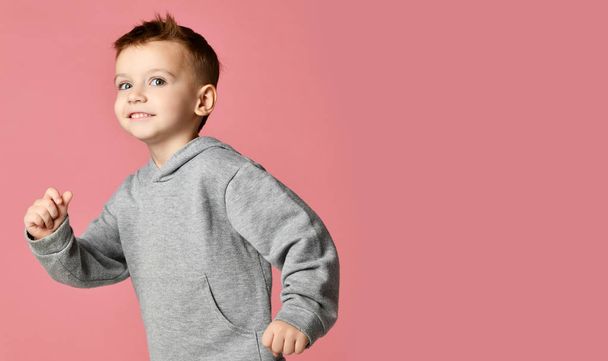 Young baby boy kid in grey hoodie with free text copy space running happy smiling on pink - Fotó, kép