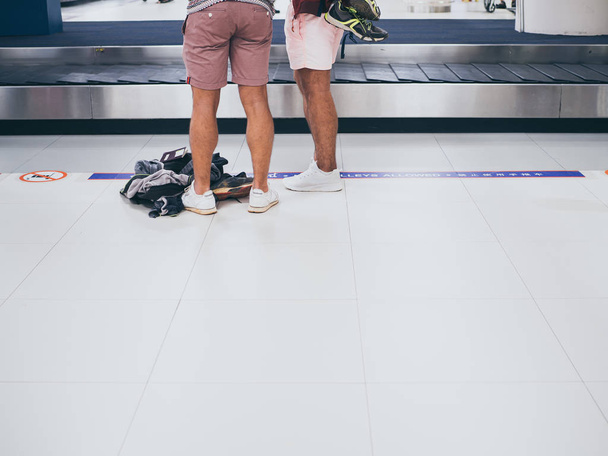 バンコク、タイ-11 月 5、2018: 2 観光客着てショート パンツやスニーカー コピー スペースとドンムアン空港のバゲージ クレームで荷物を待っています。. - 写真・画像