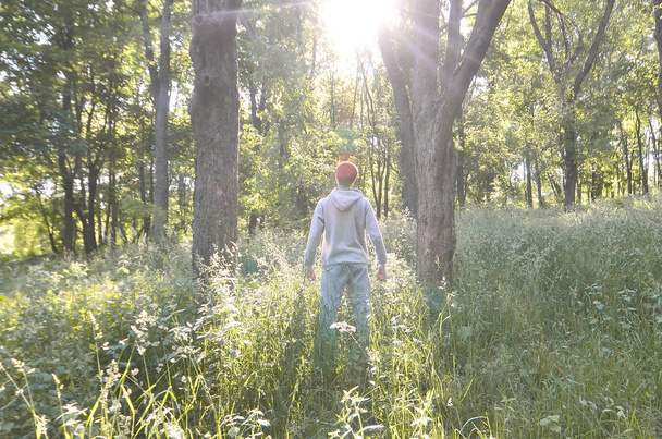 Um jovem de fato desportivo cinzento está em frente ao sol entre as árvores da floresta. Recreação durante uma corrida esportiva na floresta ao ar livre. O arrebatamento de uma bela aurora
 - Foto, Imagem