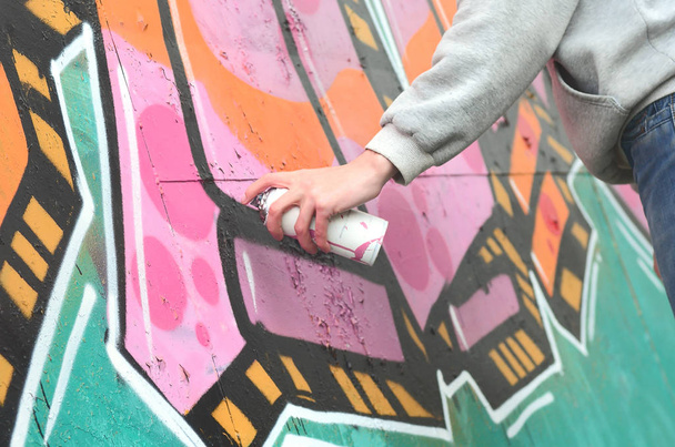 Hand of a young guy in a gray hoodie paints graffiti in pink and green colors on a wall in rainy weather - Photo, Image
