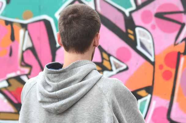 Mladá graffiti umělec v šedá mikina se dívá na zdi s jeho graffiti v růžové a zelené barvy na zdi v deštivém počasí. Koncept street artu - Fotografie, Obrázek