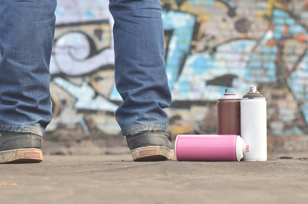 Un bodegón de varias latas de aerosol de pintura se encuentra en un revestimiento de techo en el fondo de una pared de ladrillo, sobre la que se pinta un dibujo de graffiti brillante y colorido. Artículos relacionados con el arte callejero
 - Foto, Imagen