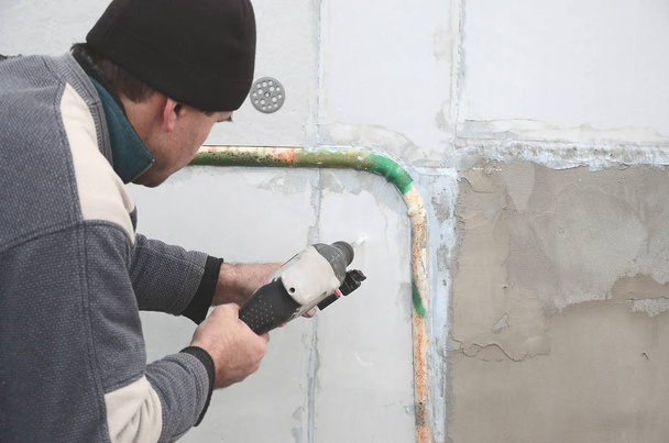 An elderly workman drills a hole in a styrofoam wall for the subsequent installation of a plastic reinforcing dowel. Creating holes in the wall with a drill. Warming of the building facade - Photo, Image
