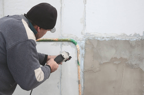 Een bejaarde workman boren een gat in een muur van piepschuim voor de latere installatie van een plastic stokje te versterken. Het creëren van gaten in de muur met een boor. Opwarming van de aarde van de gevel van het gebouw - Foto, afbeelding