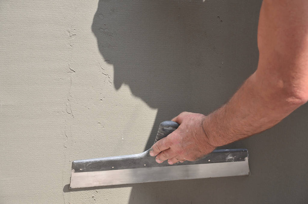 Mãos de um velho trabalhador manual com ferramentas de reboco de parede renovando casa. Estucador renovando paredes exteriores e cantos com espátula e gesso. Isolamento de parede. Acabamentos para construção
 - Foto, Imagem