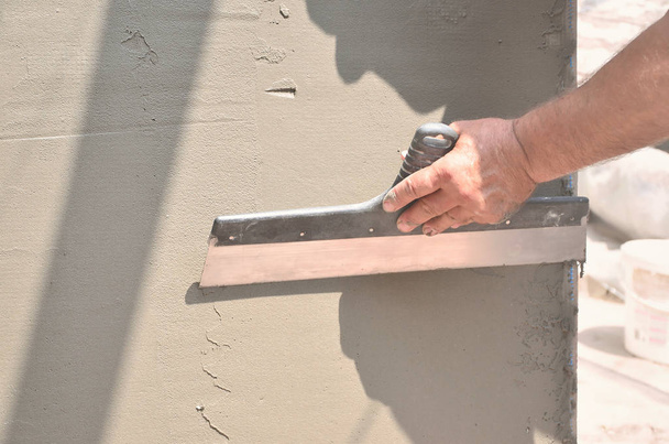 Die Hände eines alten Handwerkers mit Putzwerkzeugen renovieren das Haus. Putzer sanieren Außenwände und Ecken mit Spachtel und Putz. Wanddämmung. Bauarbeiten - Foto, Bild