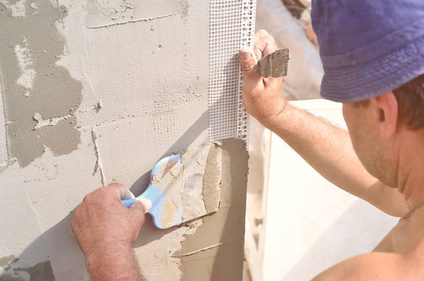 50-jähriger Handwerker mit Putzwerkzeugen renoviert Haus. Putzer sanieren Wände und Ecken mit Spachtel und Putz. Wand-Maische-Installation. Bauarbeiten - Foto, Bild