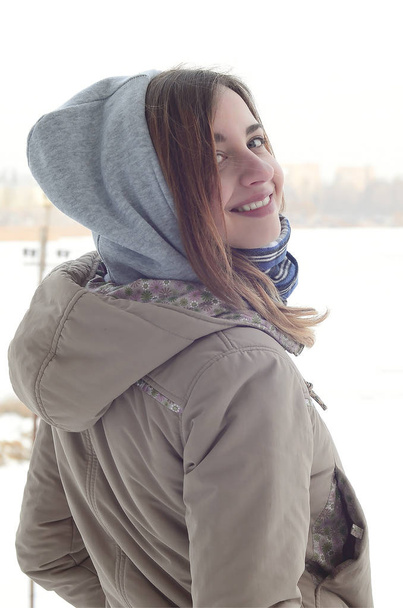 Kış döneminde ufuk çizgisi arasında gökyüzü ve donmuş göl çevresinde genç ve gülümseyen bir beyaz kız görünüyor - Fotoğraf, Görsel