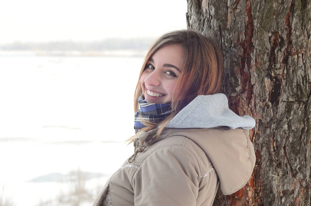 Молодая и улыбающаяся кавказская девушка зимой смотрит на горизонт между небом и замерзшим озером.
 - Фото, изображение