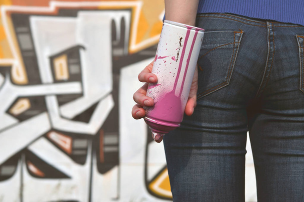 Фото руки девушки с банками аэрозольной краски в руках на фоне стены граффити. Концепция уличного искусства и использование аэрозольных красок. Изображение из магазина граффити
 - Фото, изображение