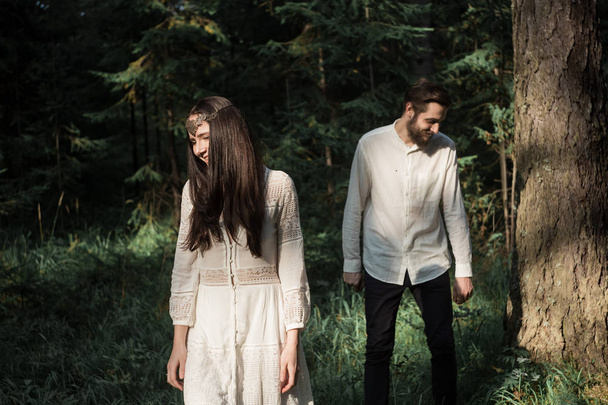 Young beautiful Slavic couple in love walks through the woods, sweet girl in a simple boho-style wedding dress. They are happy and calm. Golden hour, summer day, warm. They kiss, hug and hold hands. - 写真・画像