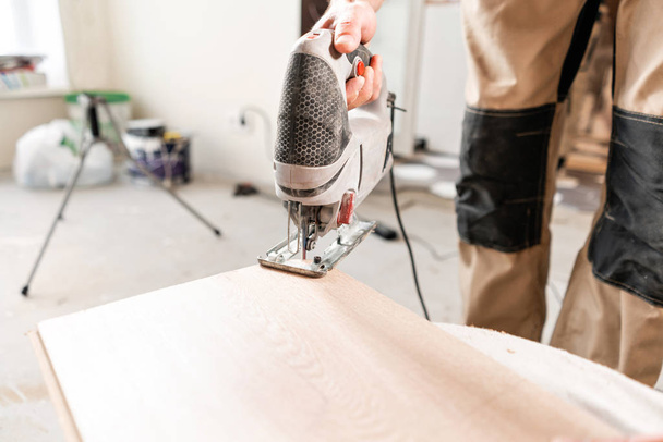 Мужчина режет доску ламината электролазерной пилой. установка нового деревянного ламината. концепция ремонта в доме
. - Фото, изображение
