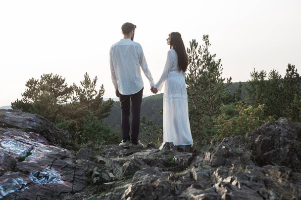 Beautiful couple in love walks in the mountains, against the backdrop of rocks, in the rays of the setting sun. A man and a woman love each other, they are gentle and happy, a love story and a wedding day. - Foto, afbeelding