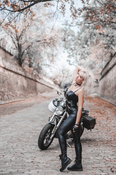 Красивая байкерша позирует с мотоциклом на дороге
.  - Фото, изображение