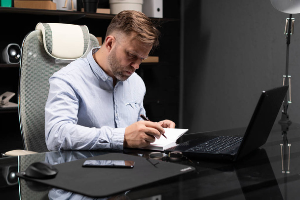 jeune homme assis à la table de l'ordinateur et prend des notes dans le journal
 - Photo, image
