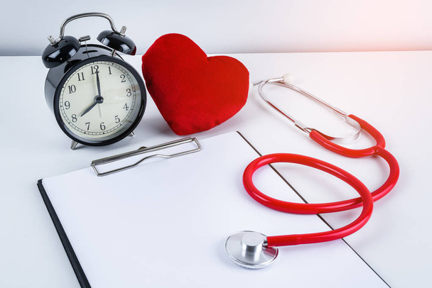 Red heart and stethoscope, alarm clock with empty clipboard on white table with copy space. Doctor Appointments concepts - Foto, Bild
