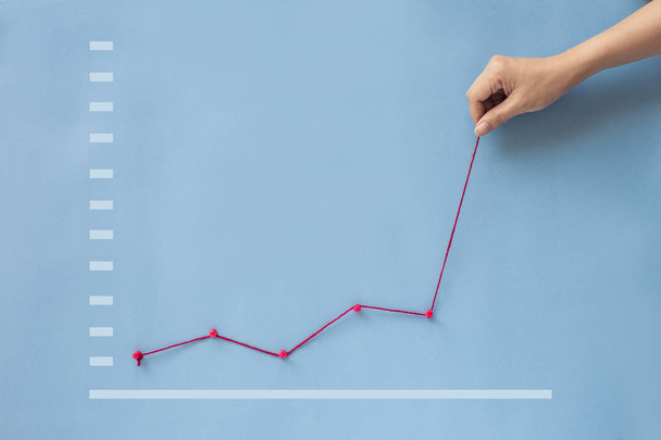 Концептуальная рука тянет график роста финансирования бизнеса вверх на синем фоне
.  - Фото, изображение