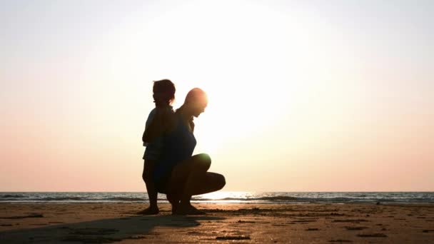 Silhueta de mãe com filha fazendo ginástica na praia ao pôr do sol
 - Filmagem, Vídeo