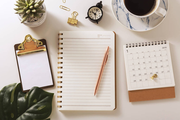 Flat lay desk with notebook, calendar, clipboard, pen and green leaf, warm tone - Фото, изображение