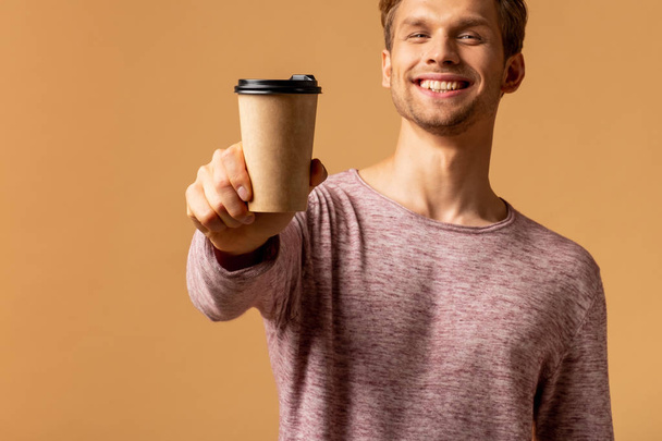Young smiling man holding cup of coffee on orange background - Фото, изображение
