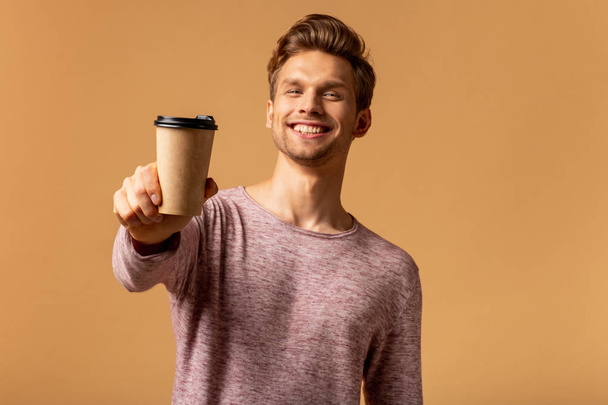 Young smiling man holding cup of coffee on orange background - Fotoğraf, Görsel