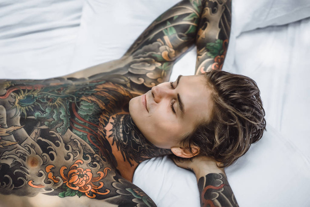 handsome young man in tattoos relaxing in bed  - Фото, зображення