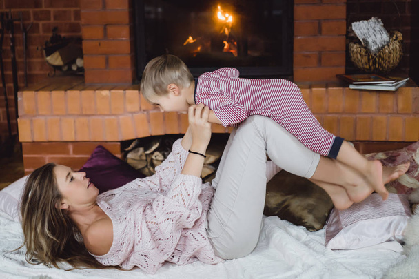 young woman with a child. Mom and son are fooling around, having fun near the fireplace. - Foto, afbeelding
