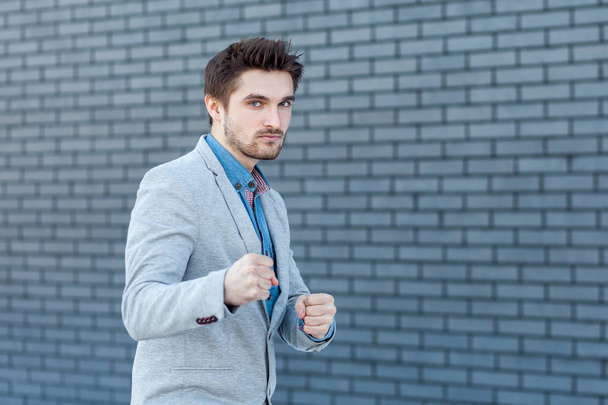 Portrait of serious handsome bearded man in casual style standing in boxing gesture and looking at camera with anger face in attack position on brick wall background. - Fotó, kép