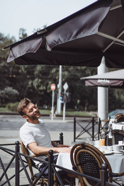 young man in a summer cafe on the terrace has breakfast - Fotó, kép