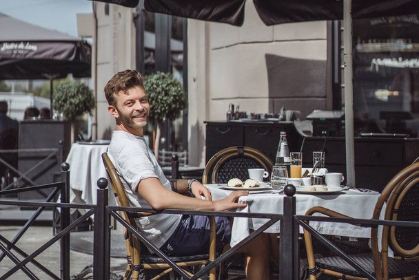 young man in a summer cafe on the terrace has breakfast - Foto, afbeelding
