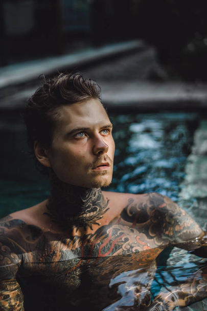 young handsome man in tattoos resting in the outdoor pool. A tattooed man in the pool is having fun. on bali, indonesia - Fotografie, Obrázek