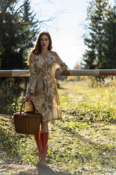 Young woman with long red hair in a linen dress gathering mushrooms in the forest in the bast basket - Foto, Bild