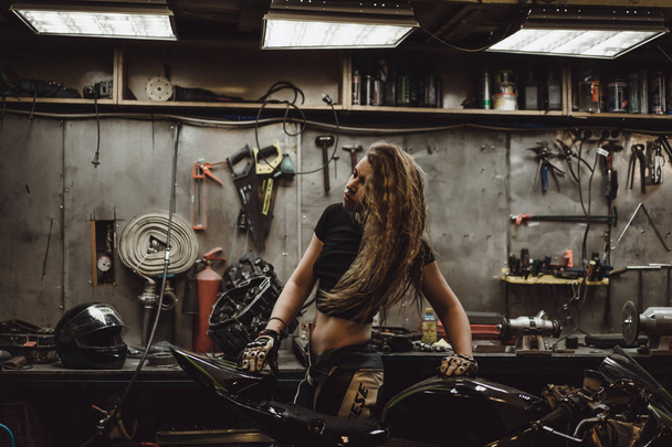 beautiful girl with long hair in the garage repairing a motorcycle - Foto, afbeelding