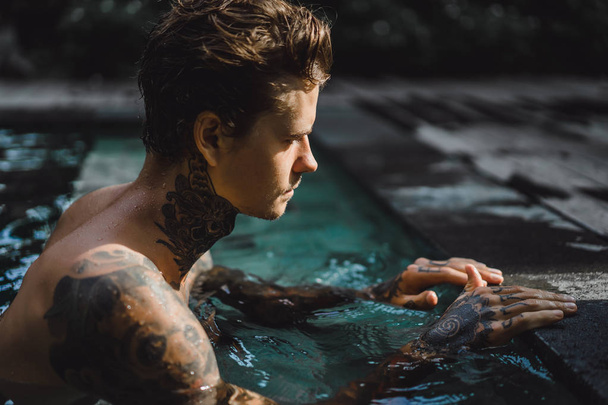 young handsome man in tattoos resting in the outdoor pool. A tattooed man in the pool is having fun. on bali, indonesia - Fotoğraf, Görsel