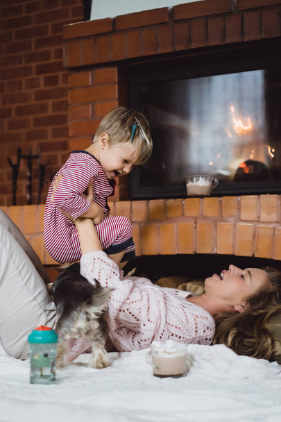 young woman with a child. Mom and son are fooling around, having fun near the fireplace. - Фото, изображение