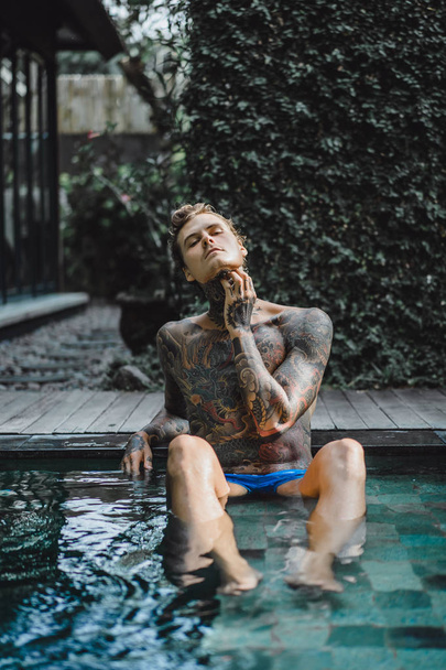 young handsome man in tattoos resting in the outdoor pool. A tattooed man in the pool is having fun. on bali, indonesia - Fotoğraf, Görsel