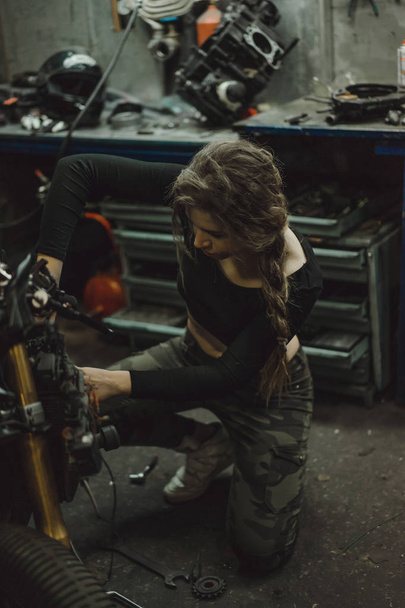 beautiful girl with long hair in the garage repairing a motorcycle - Foto, Bild