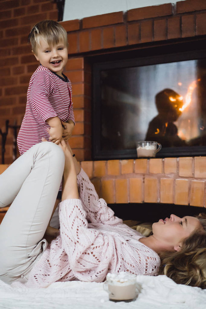 young woman with a child. Mom and son are fooling around, having fun near the fireplace. - Photo, Image