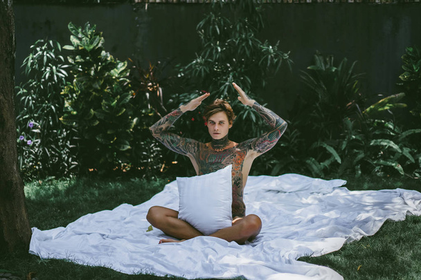 a young handsome tattooed man in the morning in bed tosses up the pillows. bed in the garden - Fotoğraf, Görsel
