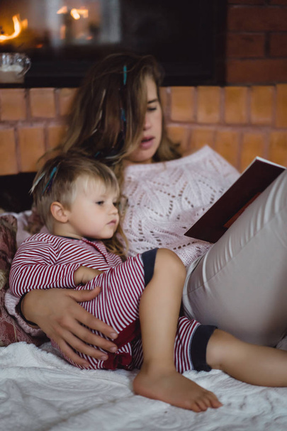 Een jonge moeder en zoon zijn het lezen van een sprookje boek bij de open haard. - Foto, afbeelding