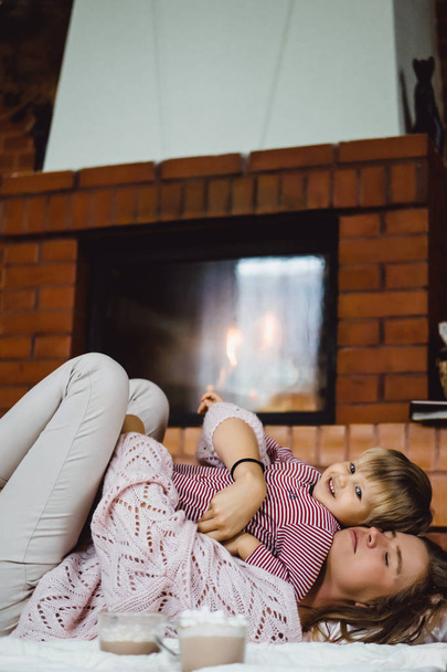 young woman with a child. Mom and son are fooling around, having fun near the fireplace. - Photo, Image