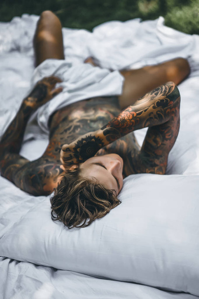 handsome young man in tattoos relaxing in bed  - 写真・画像