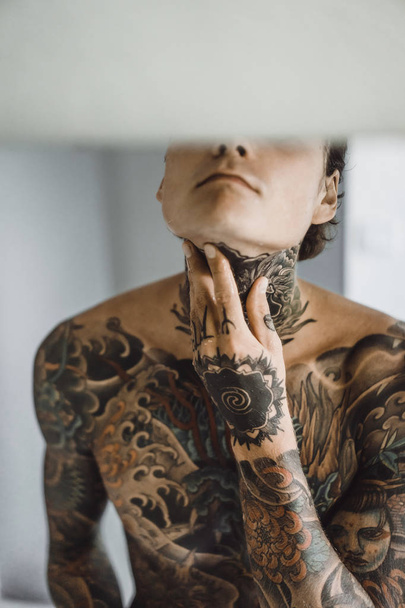 a young handsome tattooed man in the morning shaves in front of a mirror, a razor in his hands, a shave. - Foto, Imagem